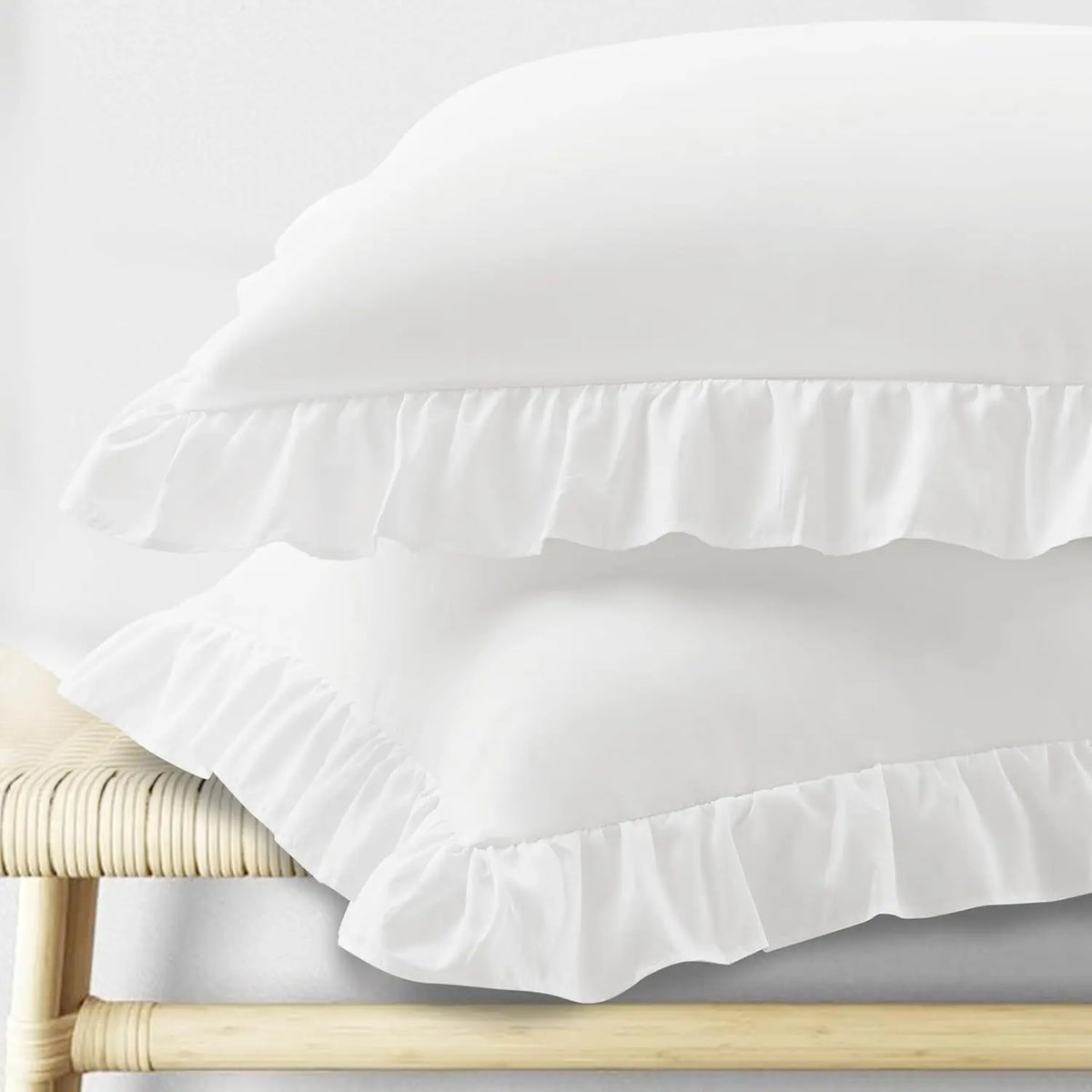 A set of two white pillow covers with ruffled envelope closures displayed on a wooden surface.