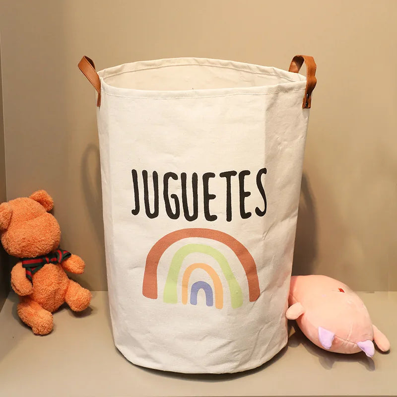 A white canvas storage basket with the word JUGUETES printed on it, featuring brown handles.