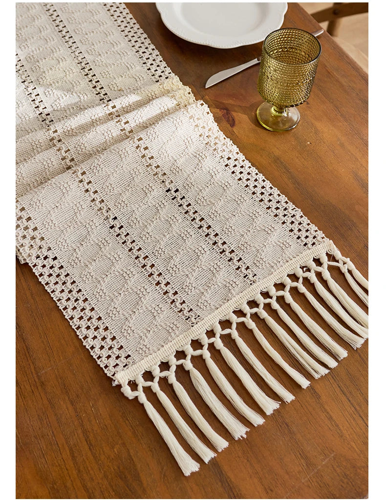 Beige boho hand-woven table runner with fringe detail on a wooden table.