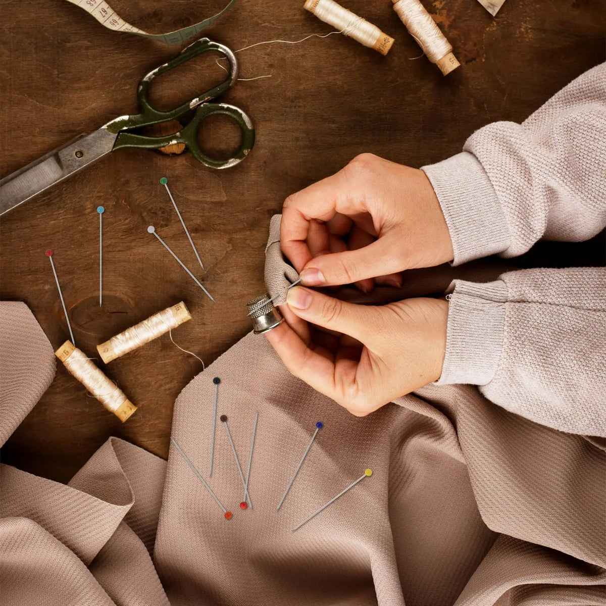 Hands are using glass head straight pins on a piece of fabric with scissors and twine for sewing or crafting.