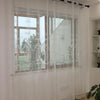 White sheer curtains with floral embroidery covering a large window in a living room setting