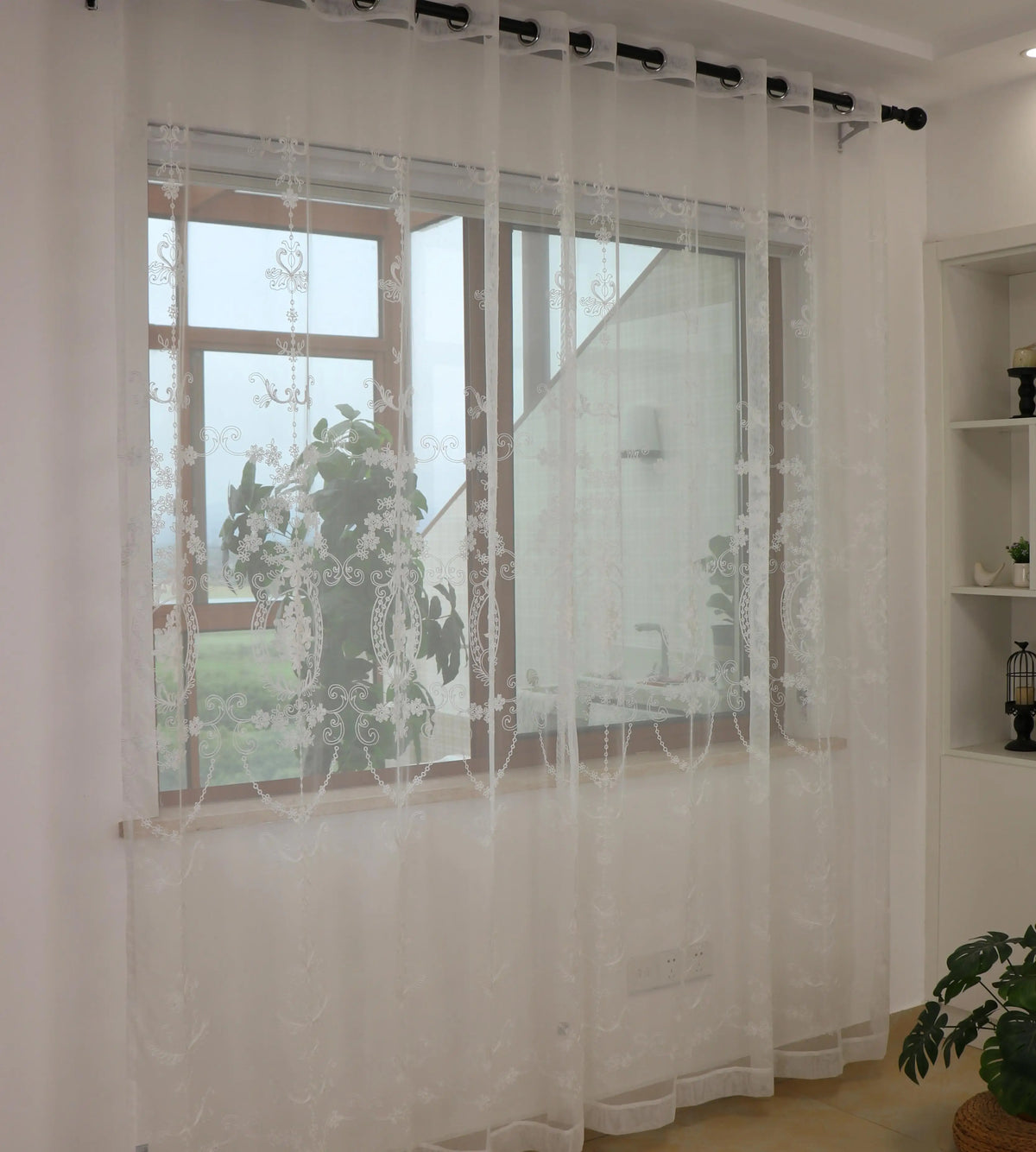 White sheer curtains with floral embroidery covering a large window in a living room setting