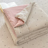 A beige striped comforter with a pink pillow is displayed on a light textured surface.