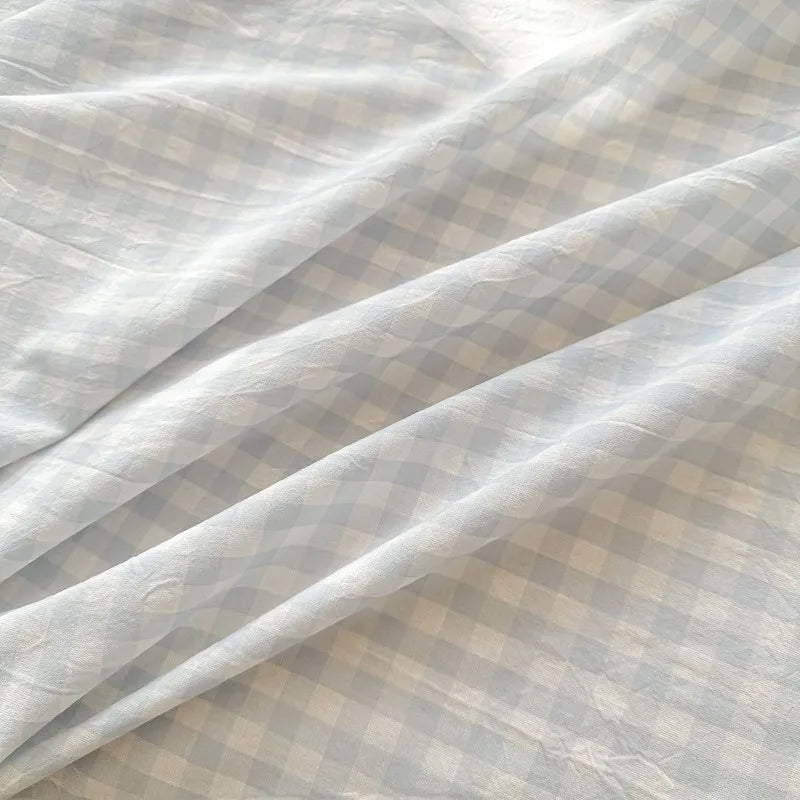 Light gray organic cotton bedding fabric with a subtle checkered pattern folded and draped.