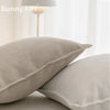 A close-up of two solid beige chenille throw pillow covers on a white surface.