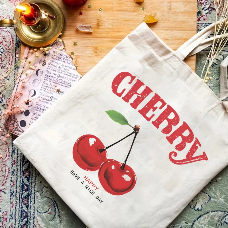 A white canvas shopping bag featuring a red cherry design and the word CHERRY printed on it, resting on a wooden surface.