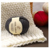 A ball of dark gray wool thread resting on a cream knitted fabric next to a red yarn ball.