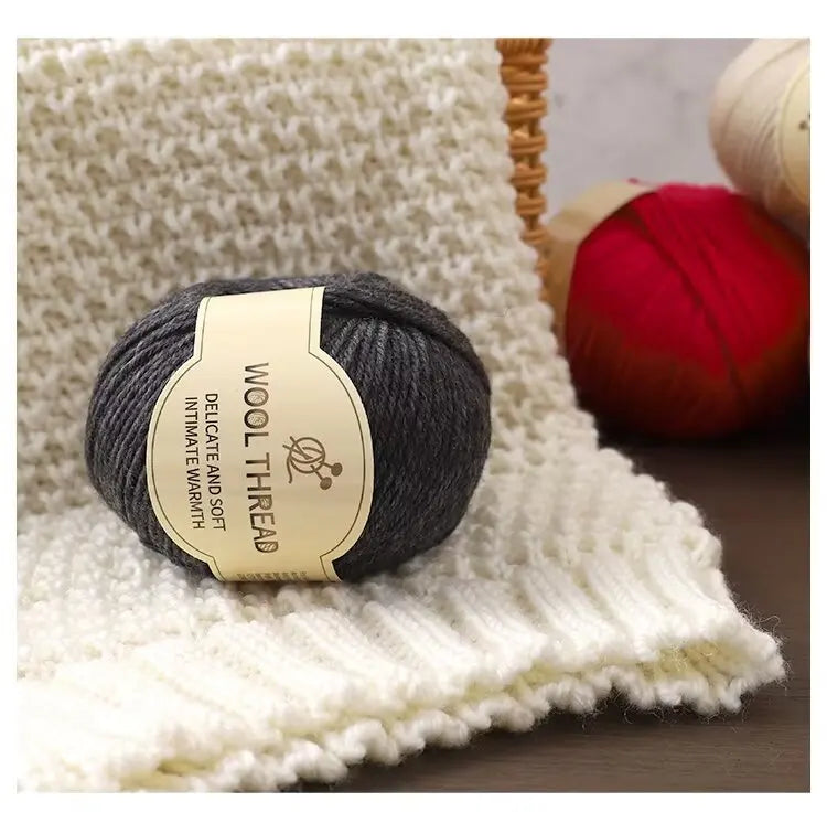 A ball of dark gray wool thread resting on a cream knitted fabric next to a red yarn ball.