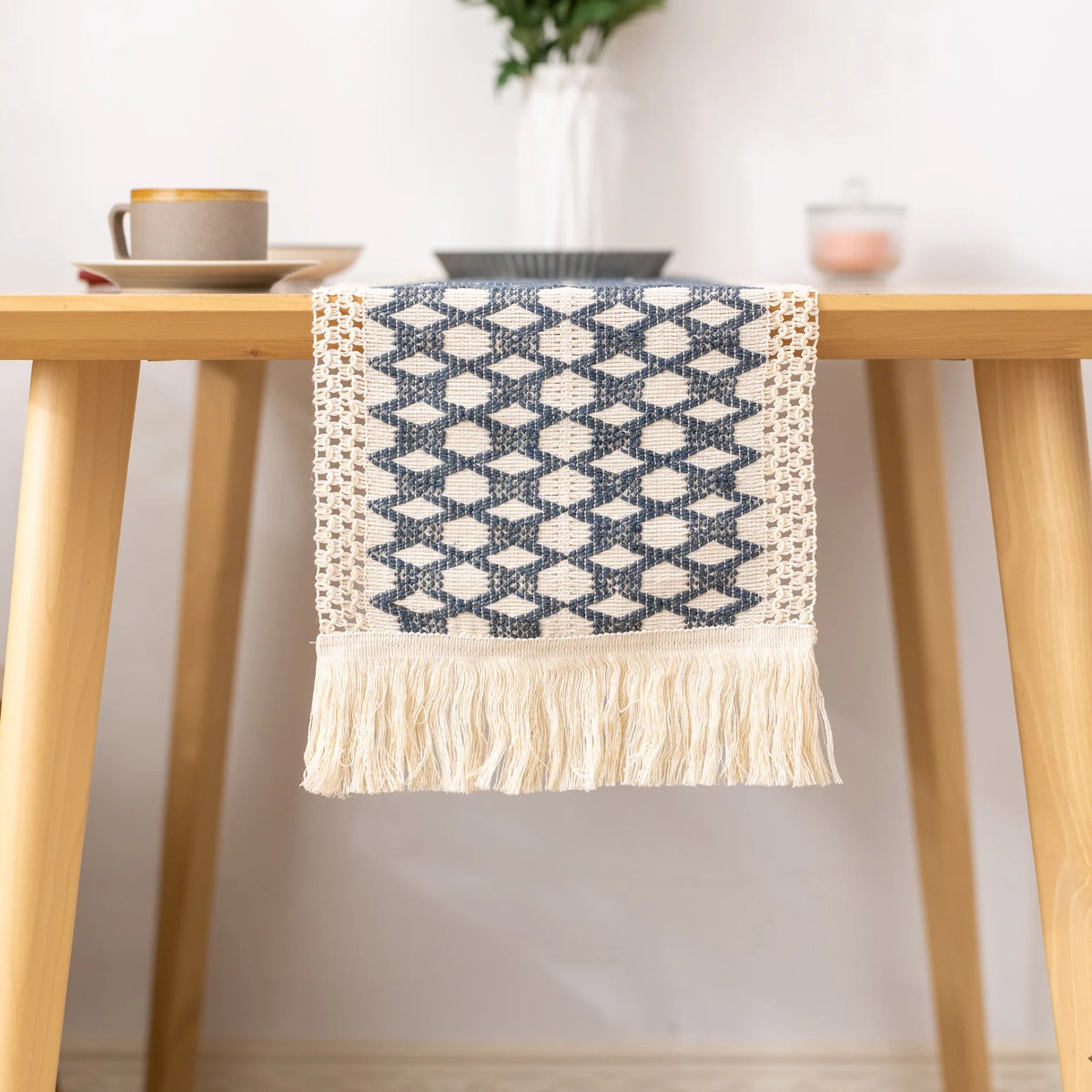 A blue and white geometric patterned linen cotton table runner with tassels displayed on a wooden table.