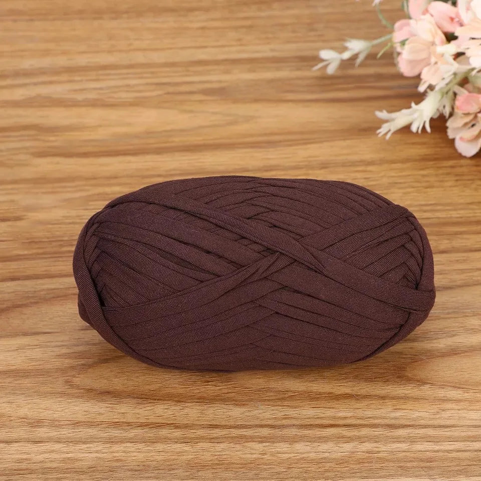 A ball of dark brown flat thread yarn lying on a wooden surface.