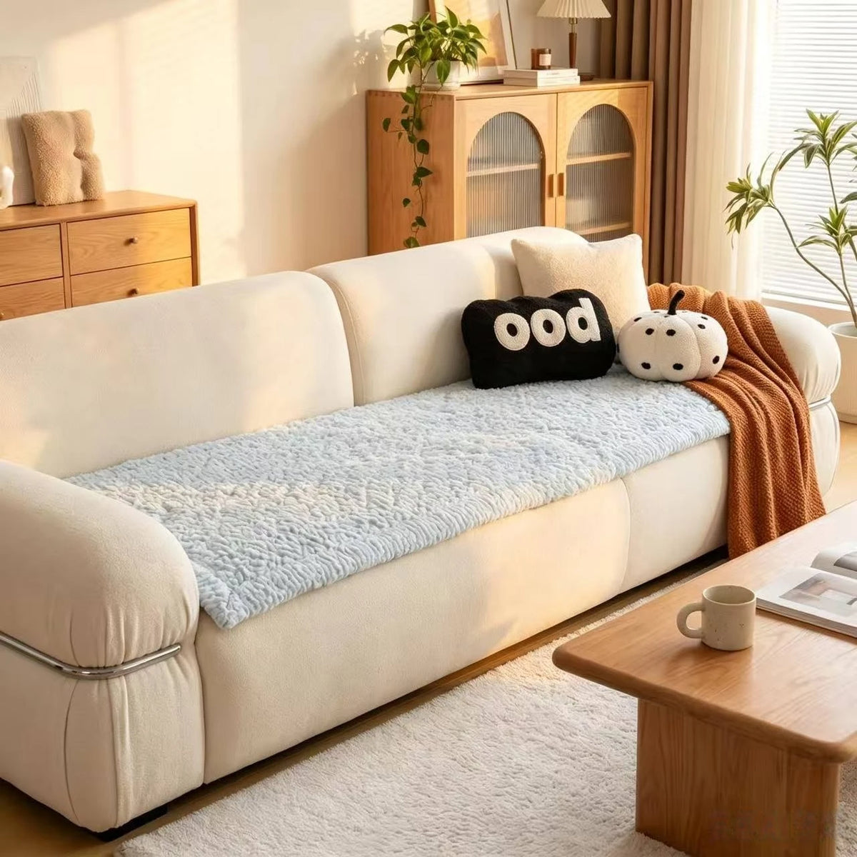 A light beige sofa with a blue quilted pad cover and decorative pillows in a bright living room.