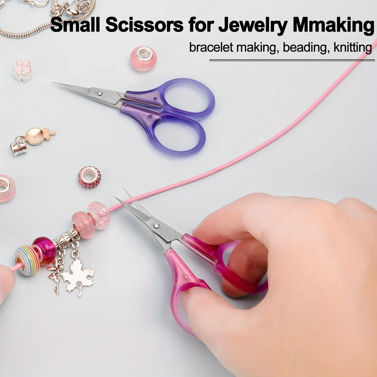 A pair of small pink precision craft scissors is shown next to various jewelry making supplies like beads and findings.