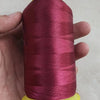 A hand holds a spool of magenta polyester sewing thread with yellow plastic end caps.