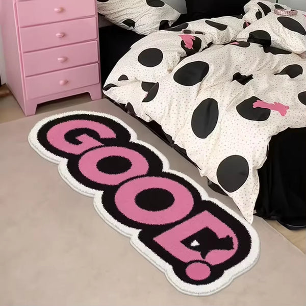 A pink and black polka dot rug with the word GOOD spelled out in pink and black embroidery