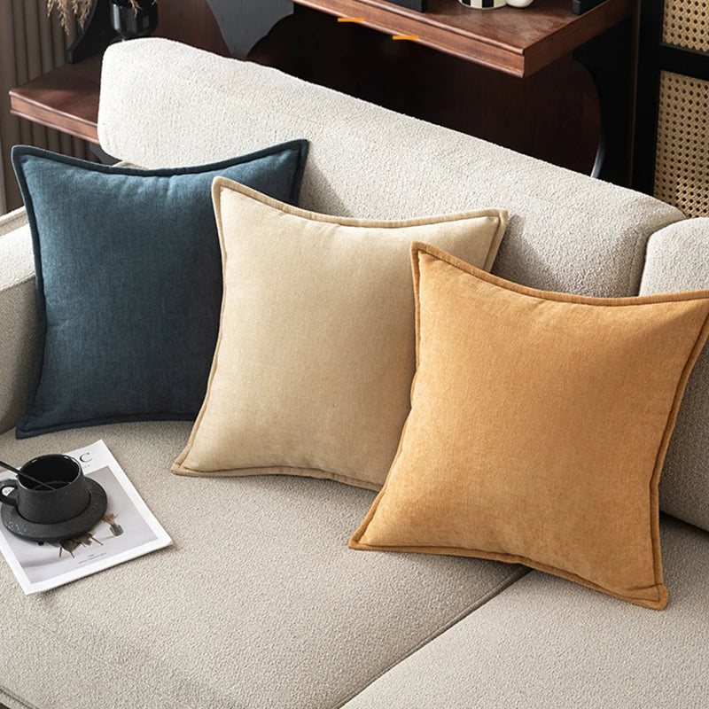 Three throw pillows in shades of dark blue, beige, and burnt orange resting on a light sofa.