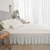 A bed featuring a light gray adjustable elastic bed skirt with a ruffled trim and white bedding.