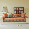 An orange chenille sofa cover with patterned pillows and a wooden display shelf featuring framed art.