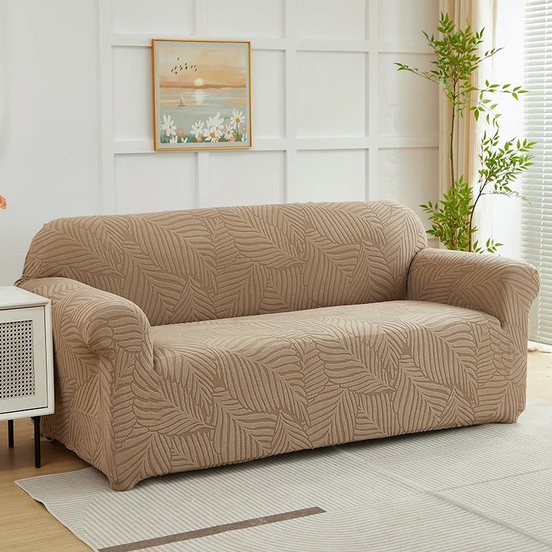 A beige jacquard leaves pattern sofa slipcover displayed on a light rug in a bright room.