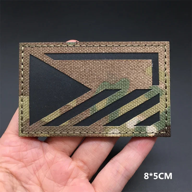 A rectangular tactical flag patch featuring a camouflage pattern on a dark background.