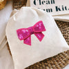 A natural linen drawstring bag with a bright pink sequin bow patch decoration.