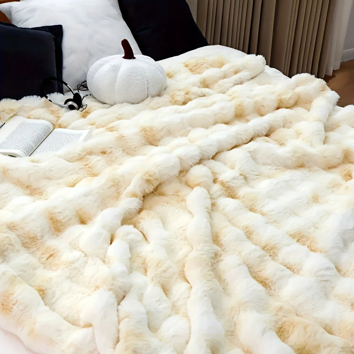 A fluffy cream faux rabbit fur throw blanket draped over a dark sofa with a white pumpkin and a book.