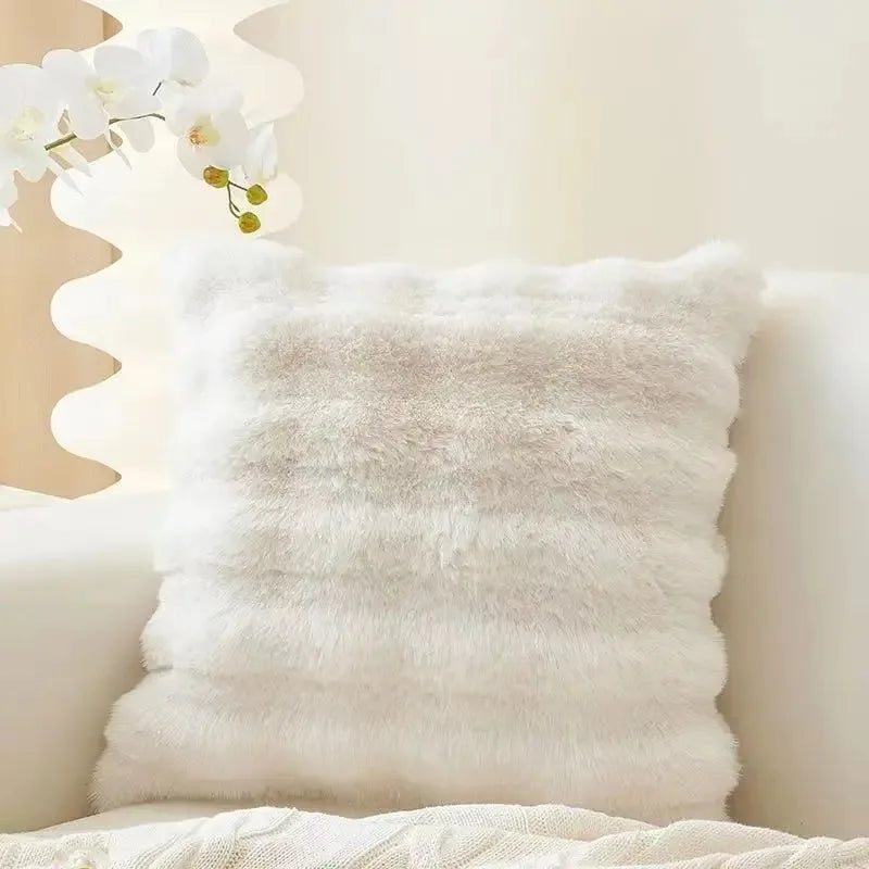 A fluffy white faux fur throw pillow resting on a light-colored surface.
