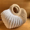 A handmade knitted storage basket in cream and beige tones sitting on a wooden surface.