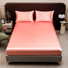 A pink satin bedding set featuring a fitted sheet and pillows displayed on a bed.