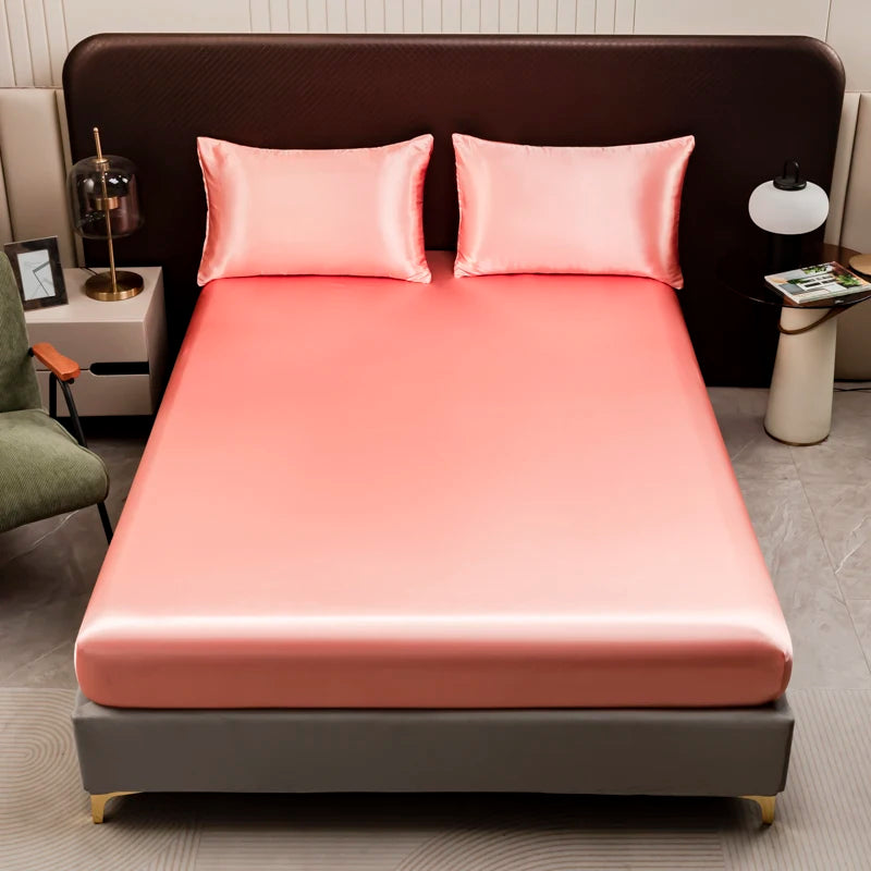A pink satin bedding set featuring a fitted sheet and pillows displayed on a bed.