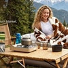 A woman is relaxing outdoors wrapped in a brown and white patterned flannel throw blanket on a wooden table.