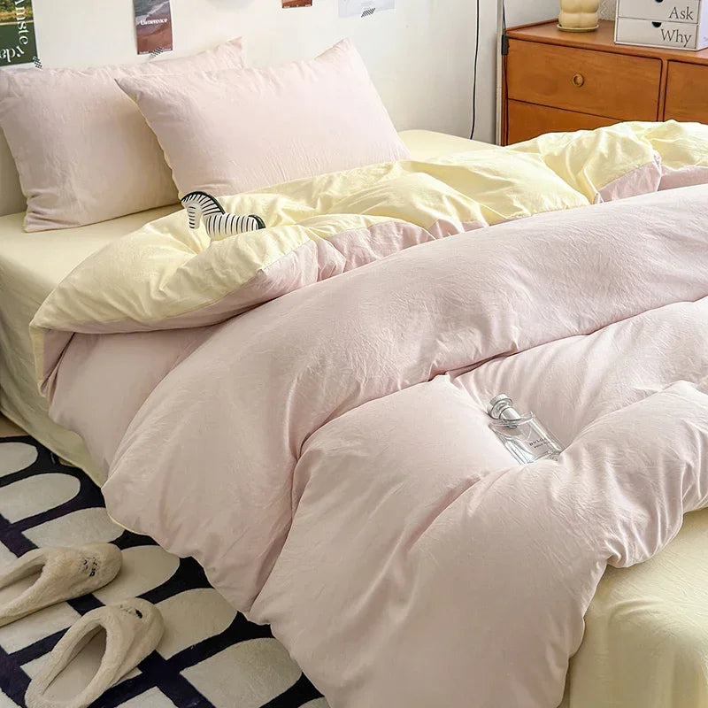 A bed with pink and cream bedding, including pillows and a duvet, next to a wooden cabinet.