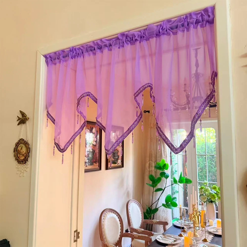 A sheer purple curtain with lace and tassels hangs in a bright room.