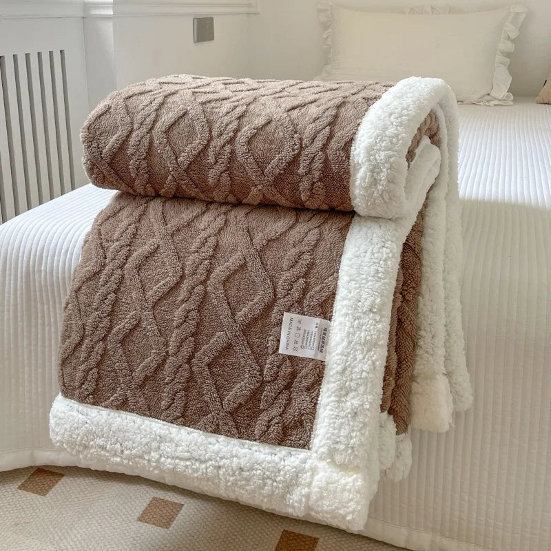 A thick brown fleece blanket with white trim is folded on a white bed, showing a diamond quilted pattern.
