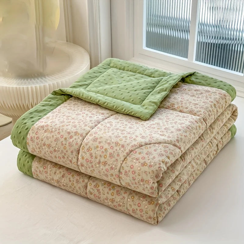 A stack of lightweight floral printed summer quilts in shades of green and beige on a white surface.