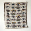 A throw blanket featuring a pattern of stylized eyes in various colors and shades on a neutral background.