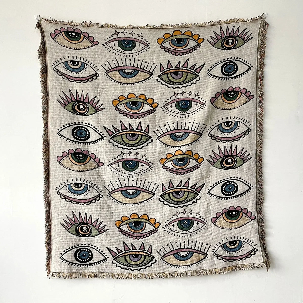 A throw blanket featuring a pattern of stylized eyes in various colors and shades on a neutral background.