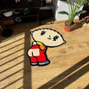 A cartoon character rug depicting a smiling, bald figure wearing a red shirt and pants on a wooden floor.