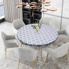 A round tablecloth with a gray and white geometric pattern is displayed on a dining table surrounded by upholstered chairs.