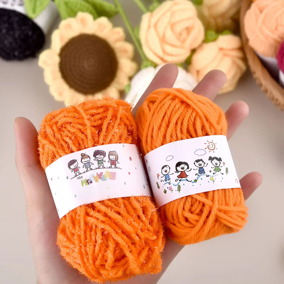 A hand holds two balls of bright orange yarn for a crochet kit with a decorative label.