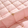 Pink quilted bed skirt with gold embroidery on a quilted fabric surface.