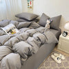 A gray duvet cover set with pillows and a folded white blanket on a bed.