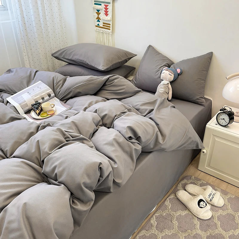 A gray duvet cover set with pillows and a folded white blanket on a bed.