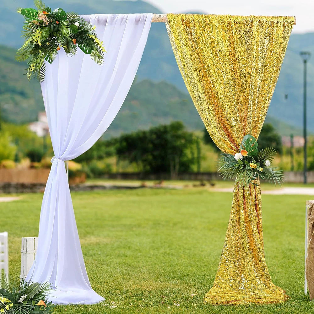 A golden sequin table runner draped between two white and gold fabric curtains outdoors
