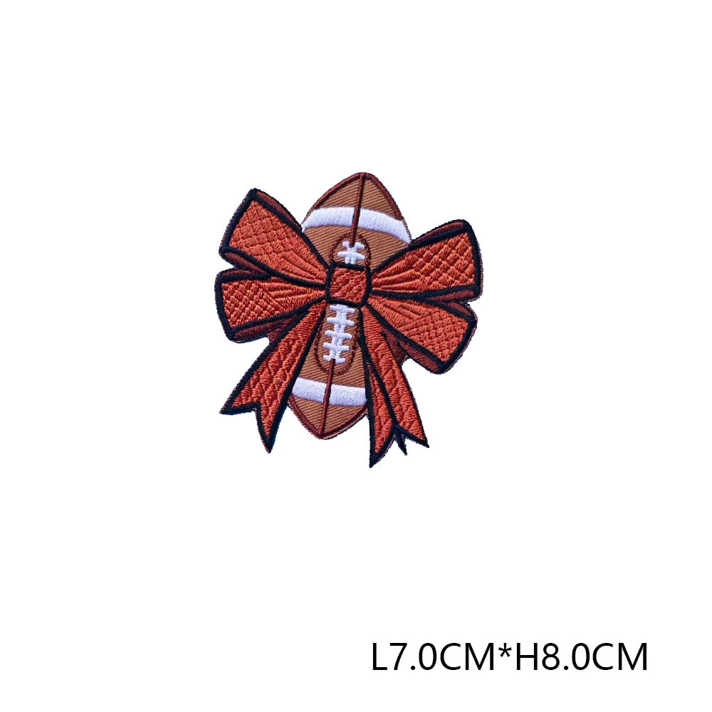 An iron-on embroidered letter patch in brown and white with a bow design.