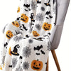A white flannel blanket featuring a Halloween theme with black bats, spiders, and pumpkins draped over a gray chair.