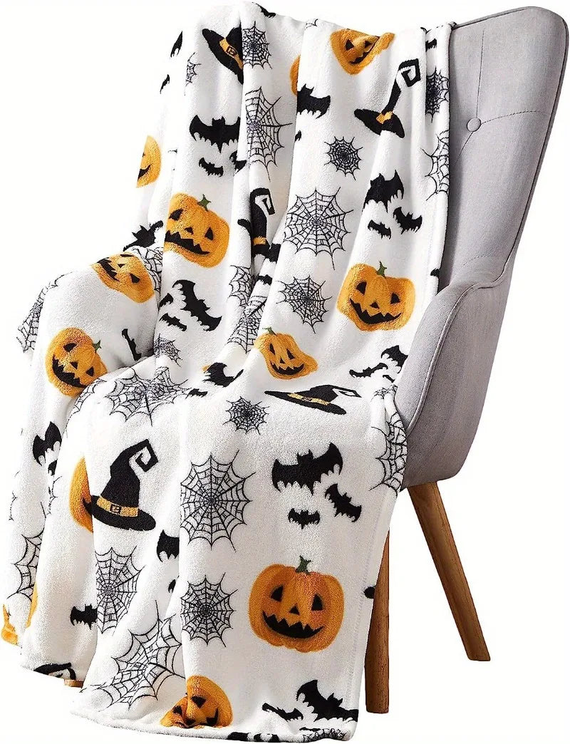 A white flannel blanket featuring a Halloween theme with black bats, spiders, and pumpkins draped over a gray chair.
