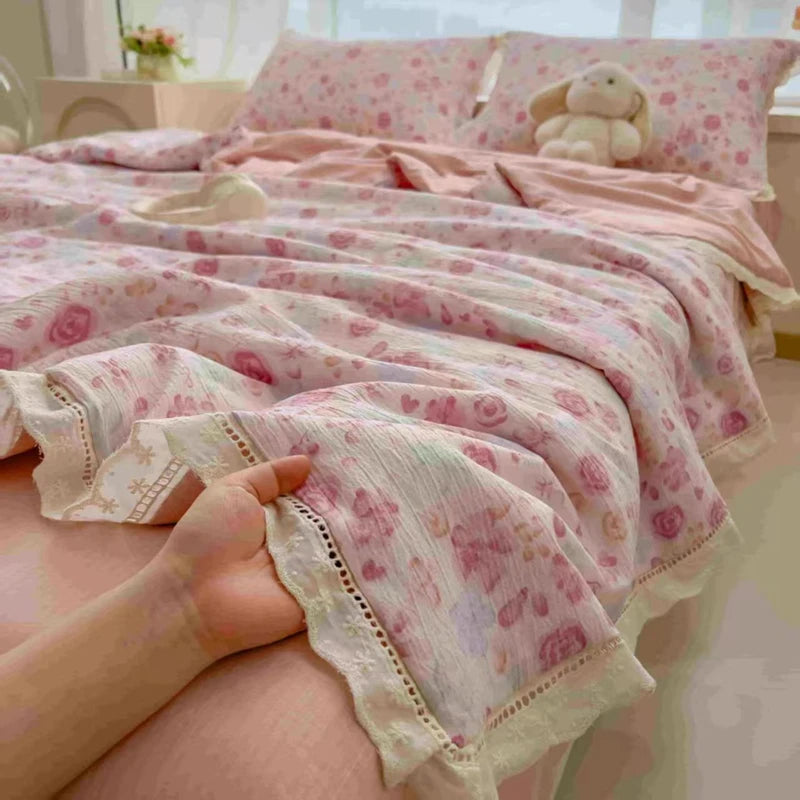 A pink and white floral print quilt blanket is draped over a bed, with a hand touching the fabric.