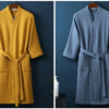 A mustard yellow cotton terry robe hanging on a wooden hanger against a dark blue wall.