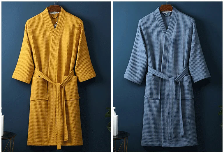 A mustard yellow cotton terry robe hanging on a wooden hanger against a dark blue wall.