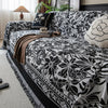 A black and white floral jacquard sofa throw blanket draped over a sofa with natural light.